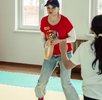 Nathalie Barth in rotem Shirt mit Löwen-Motiv leitet im Gruppentraining eine Übung mit einem Kind an